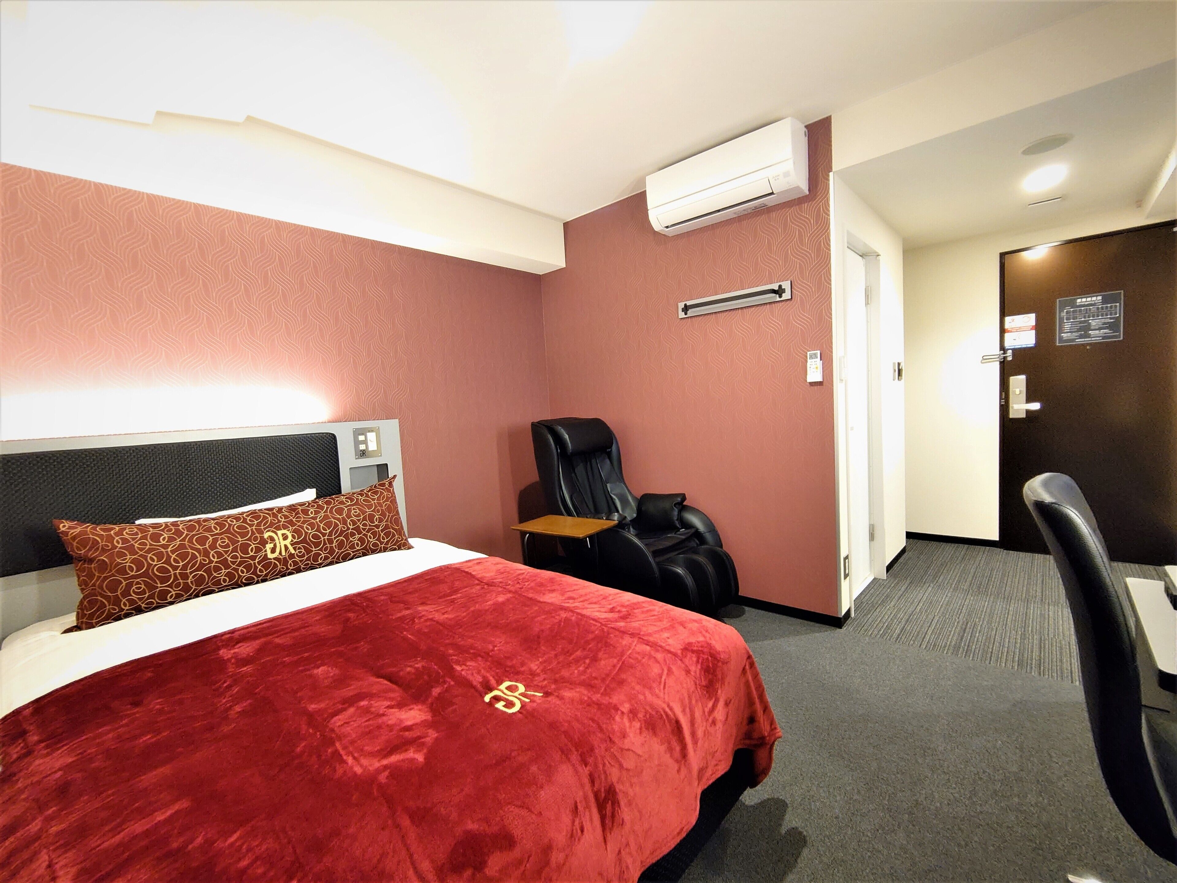 A hotel room with a bed, a massage chair, an air conditioning unit, and a door with a sign.