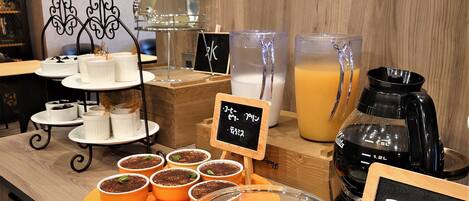 Eine Kaffeestation mit verschiedenen Getränken, darunter ein Krug Orangensaft, ein Glas mit einer Zitronenscheibe und mehrere kleine Tassen Kaffee.