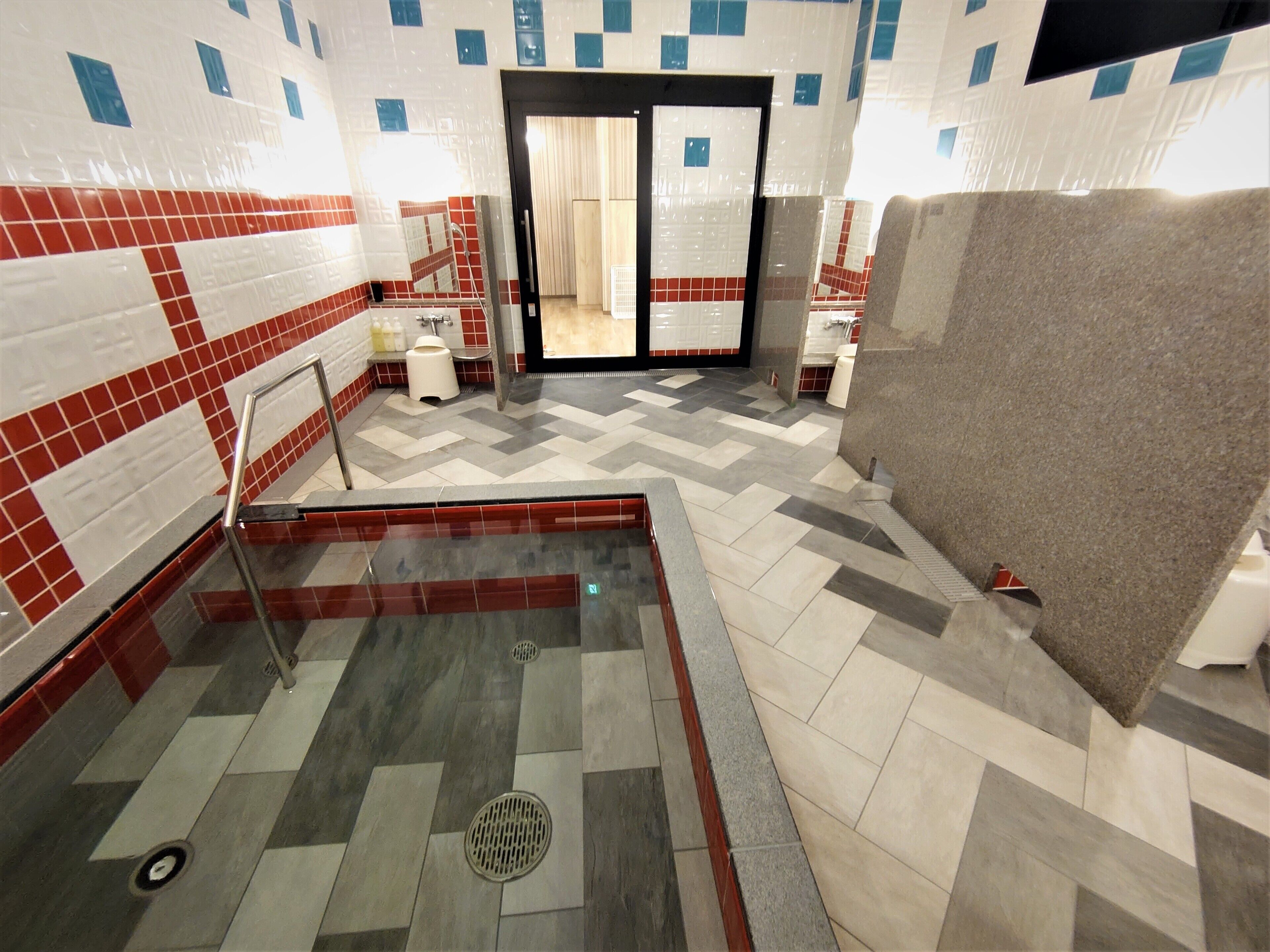 A public restroom with a tiled floor, a handrail, a toilet, and a sink.