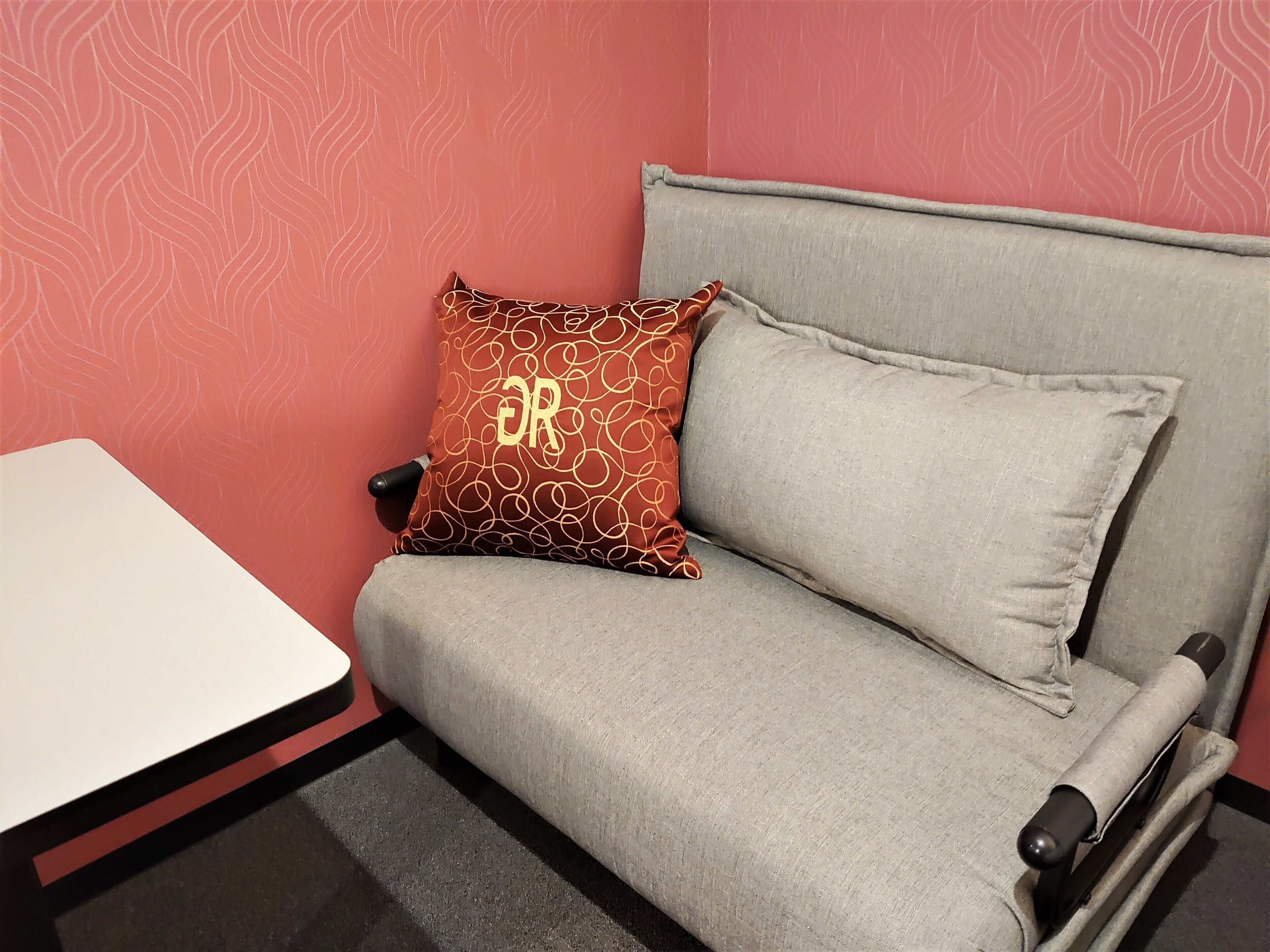 A room with a grey sofa, a red patterned pillow, and a white table.