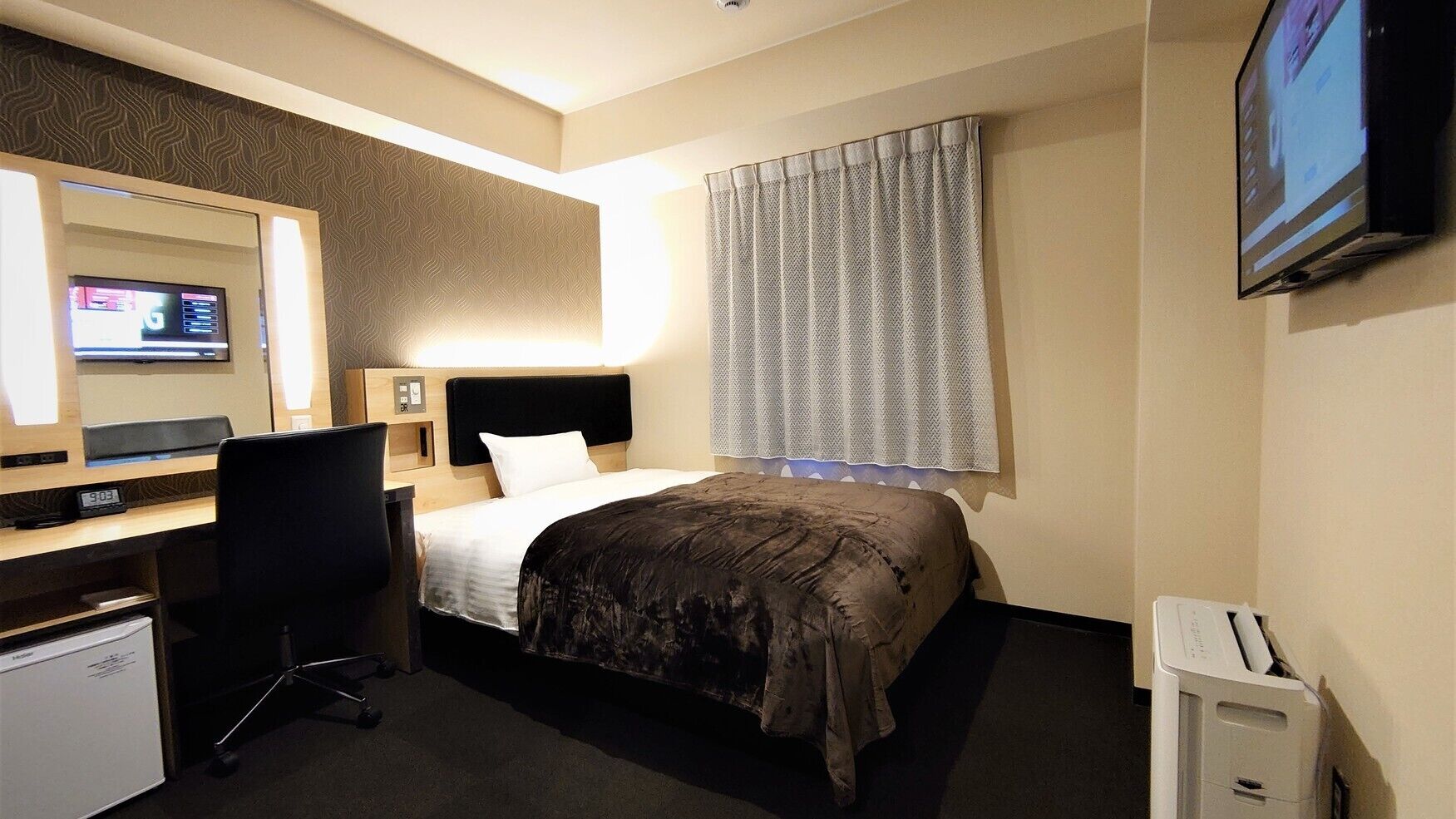 Een hotelkamer met een bed, bureau, stoel, televisie en een kleine koelkast.