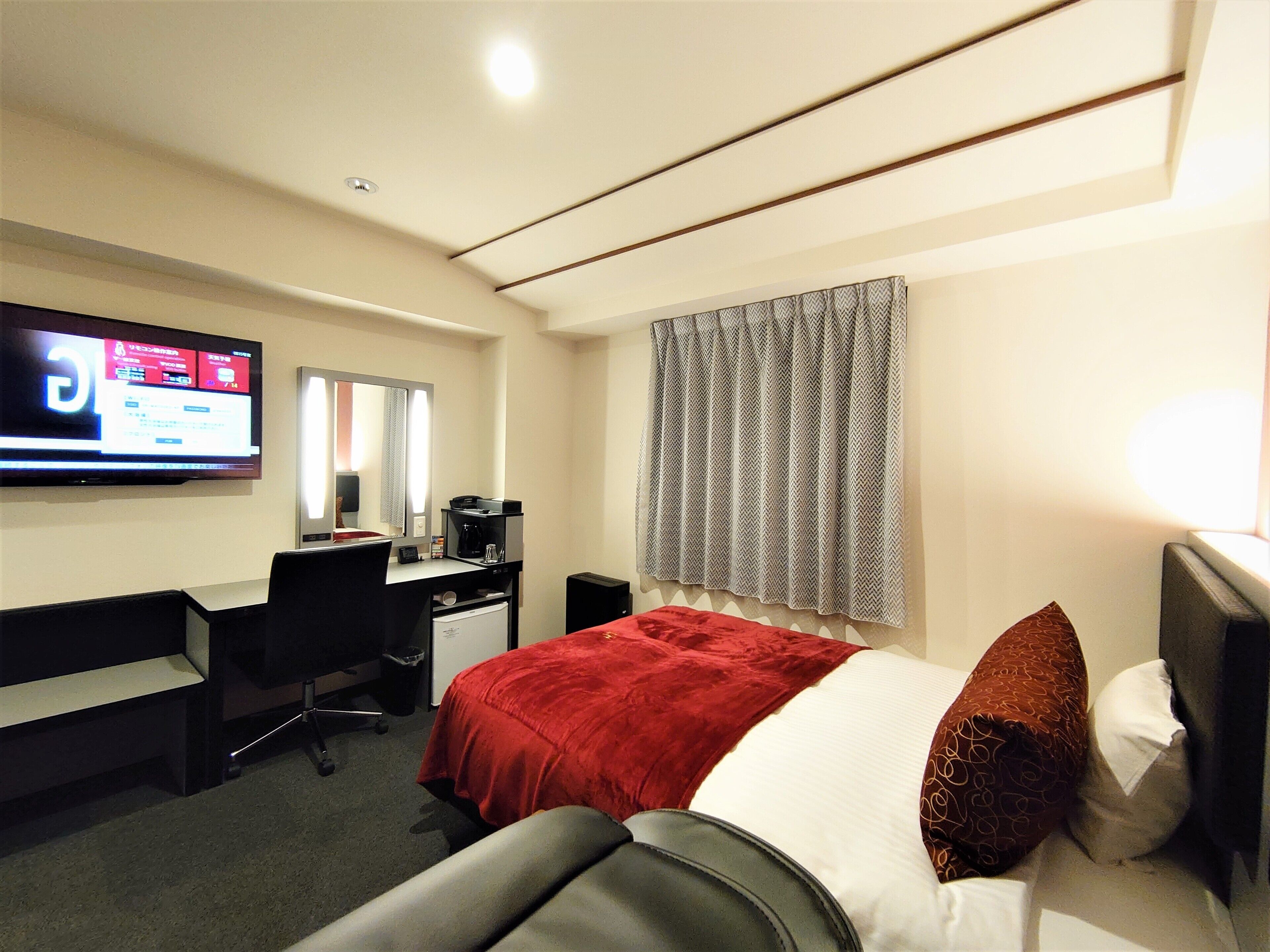 Habitación de hotel con cama, escritorio, silla, televisión y ventana con cortinas.