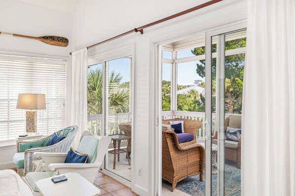 A bright room with white walls, a large window, and a wicker chair.