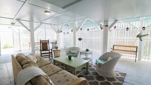 A covered patio with wicker furniture, a table, and a bench.