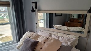 A bedroom with a bed, a window with curtains, a bedside lamp, and a mirror on the wall. - Tina's bungalow  (Manitowoc)