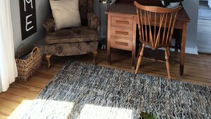 A cozy room with a dark brown armchair, a wooden desk, and a wall-mounted sign that reads "WELCOME TO OUR HOME EST. 1812". - Tina's bungalow  (Manitowoc)