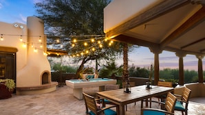 Un patio exterior con mesa de billar, sillas de madera y luces colgantes.