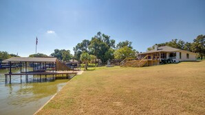 A lakeside property with a dock, grassy area, and a house with a porch. - Private Dock & Slip: Cedar Creek Reservoir Home (Mabank)