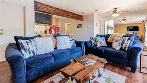 A modern living room with two blue sofas, a wooden coffee table, and a kitchen area in the background. - Hike In/Out w/Unforgettable Views+ Hot Tub-W/D in Unit-Mini Arcade-Fireplace-Deck (Steamboat Springs)