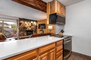 A kitchen with wooden cabinets, a stone wall, a built-in microwave, a stove, and a television.
