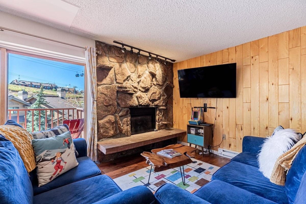 A living room with a stone fireplace, a flat-screen TV, and blue sofas.