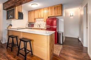 Una cocina con armarios de madera, un refrigerador rojo, un taburete de bar y una pizarra con la palabra 'WELCOME!'.