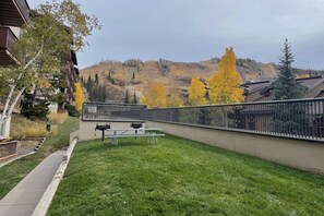 Ein grasbewachsenes Freigelände mit Picknicktisch und Bänken, einem Metallzaun und Blick auf eine hügelige Landschaft mit herbstlich gefärbten Bäumen.