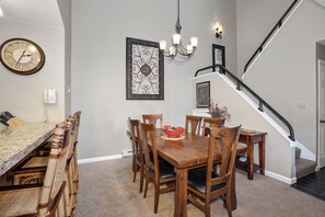 A dining area with a wooden table and chairs, a chandelier, and a staircase.