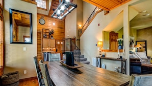 Un'ampia sala da pranzo con un grande tavolo di legno, una scala che conduce a un piano superiore e una zona salotto accogliente con un divano.