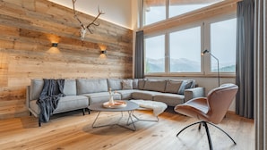 A modern living room with a wooden wall, a large window, and a sofa. - Luxurious and beautiful lodge with fantastic view (Turracher Höhe)