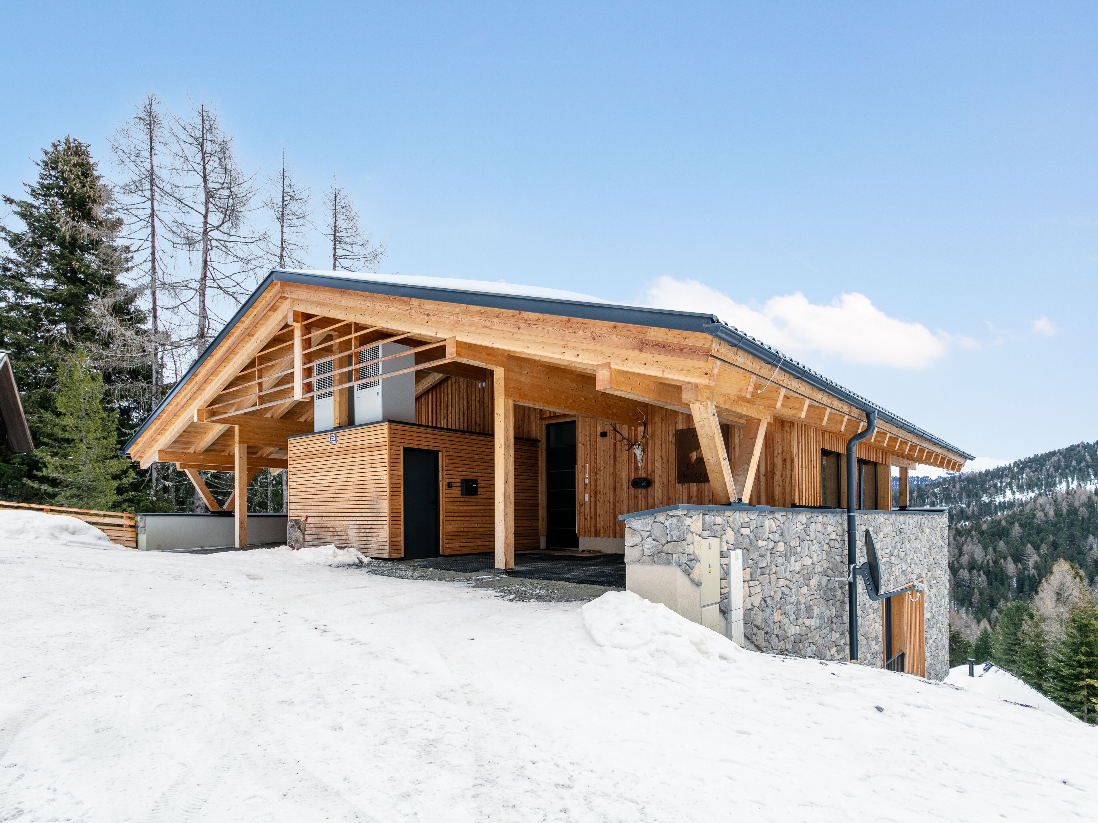A modern wooden cabin with a stone foundation, large windows, and a covered entrance area.