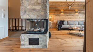A cozy living room with a stone fireplace, wooden beams, and a stone wall. - Luxurious and beautiful lodge with fantastic view (Turracher Höhe)