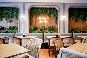 Un interior de restaurante con cabinas, mesas, sillas de mimbre y un letrero de neón en la pared.