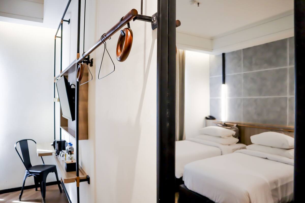 A hotel room with a desk, chair, and two beds.