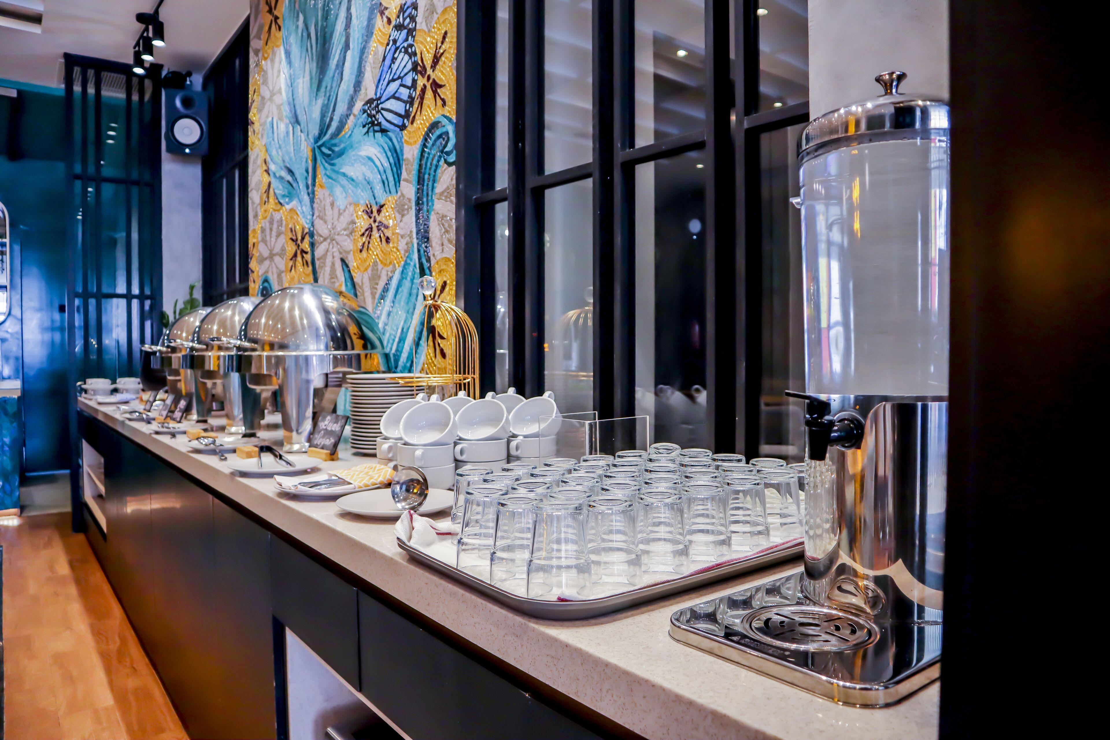 A buffet setup with clear glassware, a coffee machine, and a decorative wall.