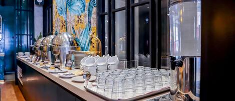 A buffet setup with clear glassware, a coffee machine, and a decorative wall.