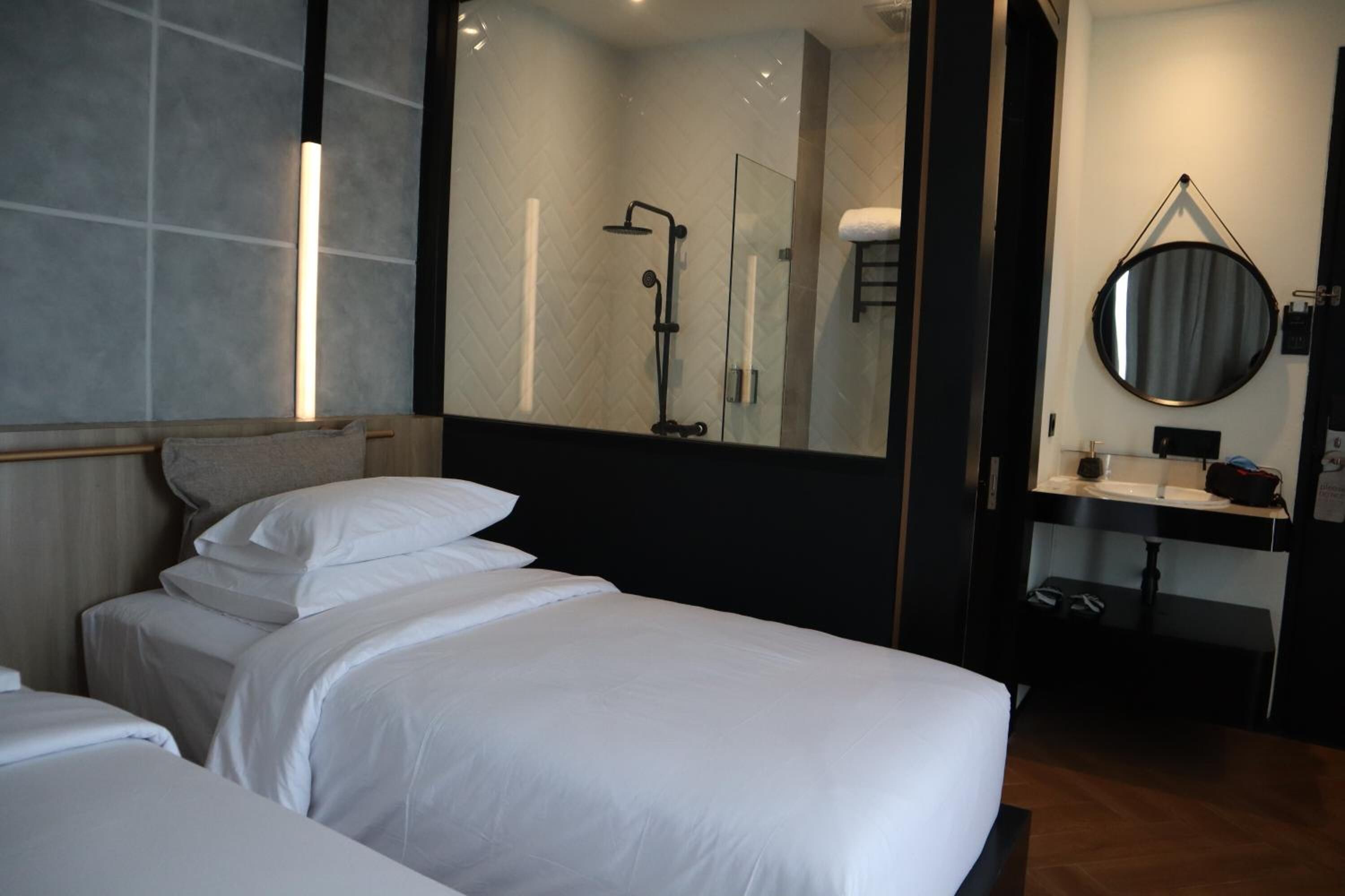 A modern hotel room with a large bed, a separate bathroom with a shower, a round mirror, and a small vanity.