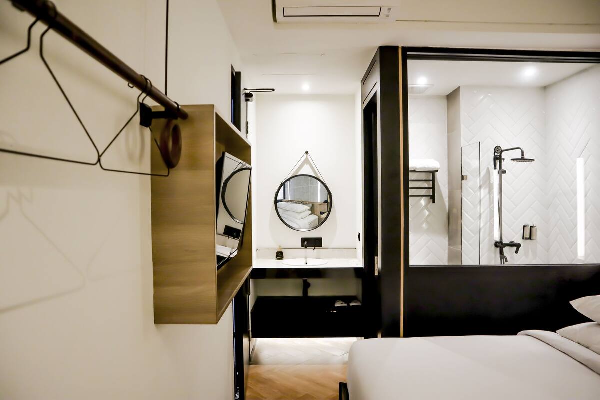 A hotel room with a bed, a bedside table, a mirror, a hanging towel rack, and a shower area.