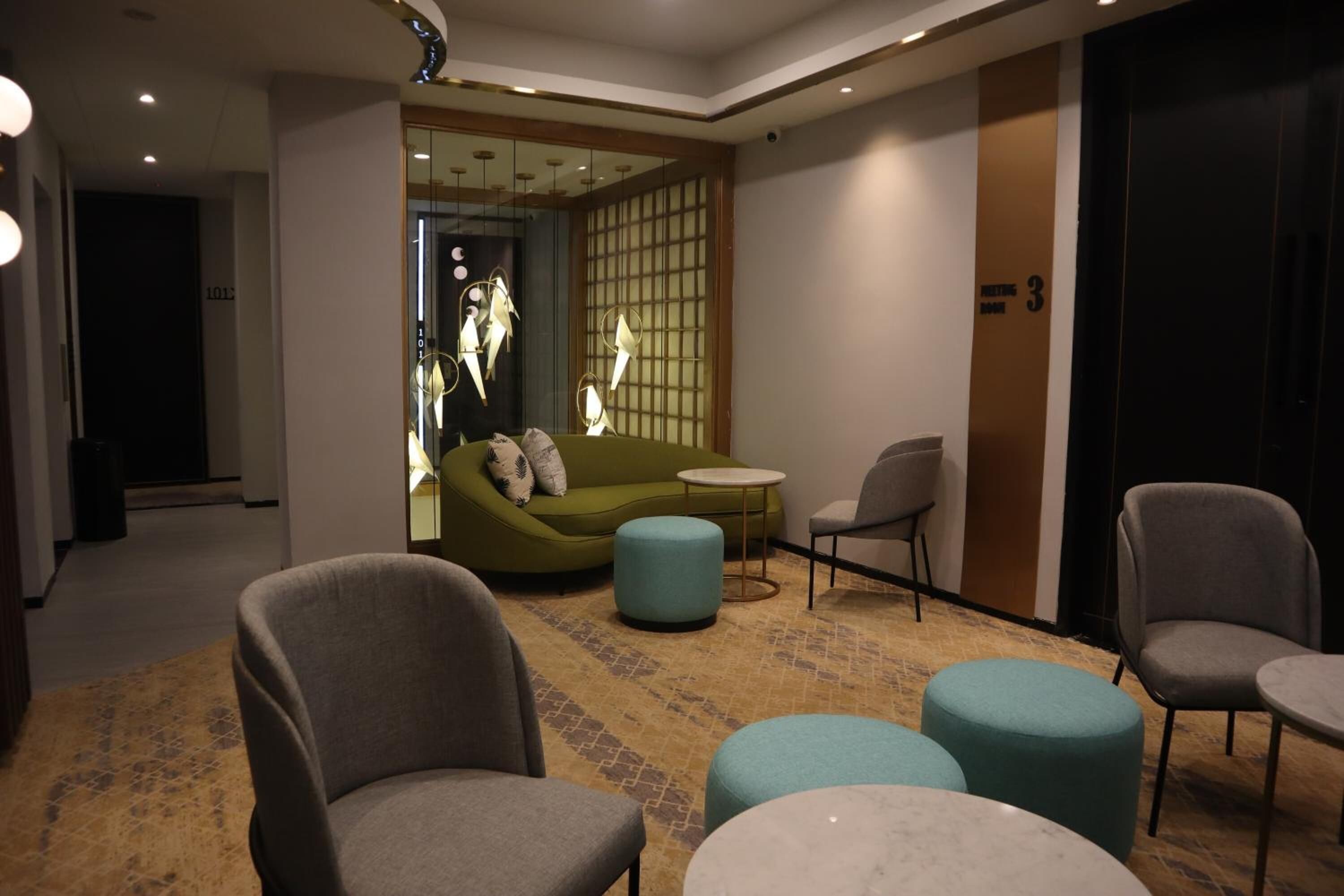 A modern hotel lobby with a green sofa, grey armchairs, and teal ottomans.