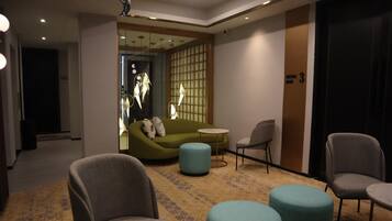 A modern hotel lobby with a green sofa, grey armchairs, and teal ottomans.
