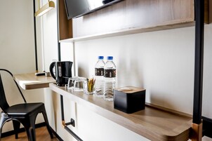 Habitación de hotel con escritorio de madera, dos botellas de agua, cafetera, caja de pañuelos y una silla.