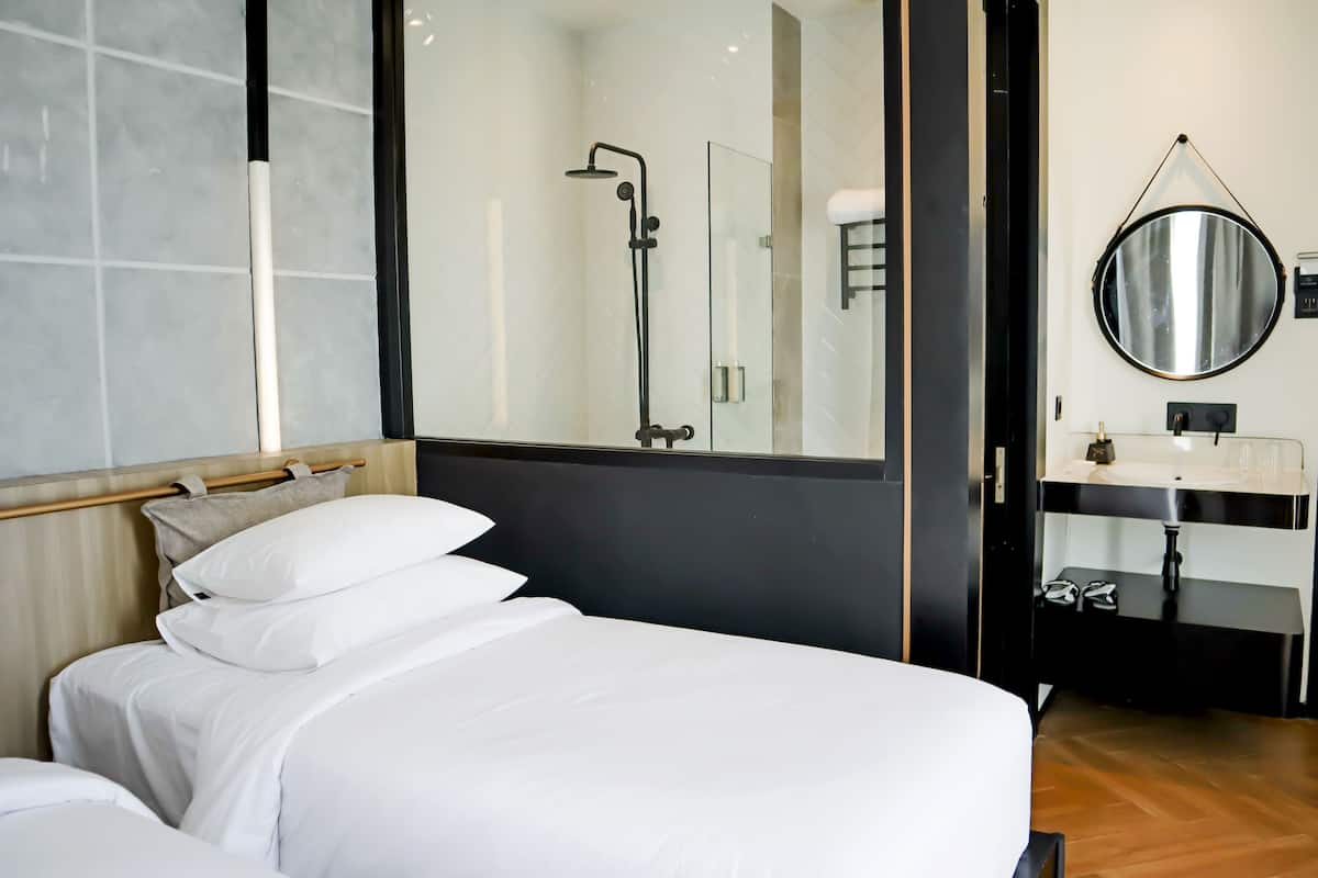 A hotel room with a bed, a large mirror, a shower, and a sink.