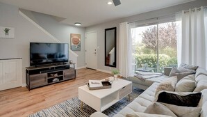 A modern living room with a flat-screen TV, a white sofa, a coffee table, and a large window with curtains. - Camelback Casa | Old Town Scottsdale | New Remodel (Scottsdale)