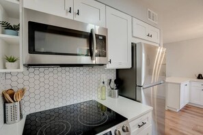 A modern kitchen with white cabinets, a black stove, a stainless steel microwave, and a refrigerator.