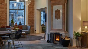 A cozy living room with a fireplace, a sofa, a dining table, and a large window with a view of a cityscape. - Studio - VIA's Appartements am Postplatz (Görlitz)
