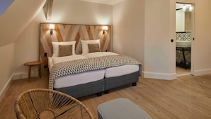 A bedroom with a wooden headboard, a bed with patterned bedding, a small bedside table, and a wicker chair. - Superior apartment - VIA's Appartements am Postplatz (Görlitz)