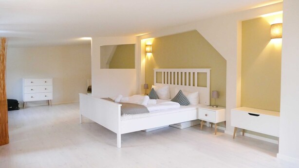 A modern bedroom with a white bed, bedside tables, and a mirror.