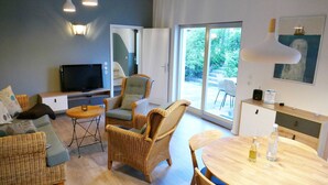 A modern living room with wicker furniture, a flat-screen TV, and a dining area with a wooden table.
