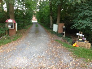 Ein Feldweg, gesäumt von Bäumen und einem Wegweiser zu Erzeugnissen.