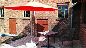 Eine Terrasse mit Tisch und Stühlen, einem roten Sonnenschirm und einem Backsteinhaus im Hintergrund.