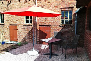 A patio area with a table and chairs, a red umbrella, and a brick building in the background. - Schlafkoje Kleine Wolke - Schäfchenwolke Apartment auf dem Bauernhof (Worpswede)