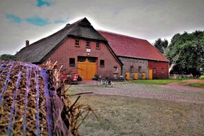 A brick building with a red roof, a large wooden door, and a bicycle parked outside. - Schlafkoje Kleine Wolke - Schäfchenwolke Apartment auf dem Bauernhof (Worpswede)