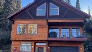 A two-story log cabin with a garage, large windows, and a balcony with skis. - ❄Ski in/out❄- Best Group Rental on Schweitzer-  Book now for holidays! (Sandpoint)