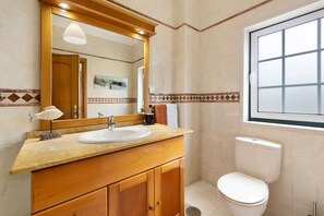 A bathroom with a wooden vanity, a sink, a mirror, a toilet, and a window.