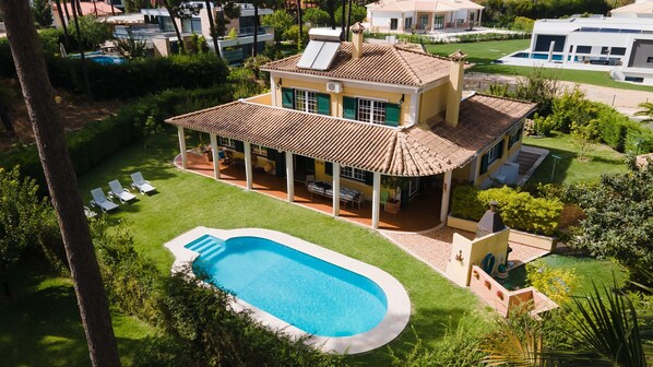A two-story house with a swimming pool, a covered patio, and a well-maintained lawn.