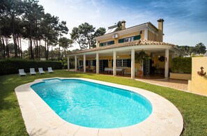 A two-story house with a swimming pool, a covered patio, and a garden.