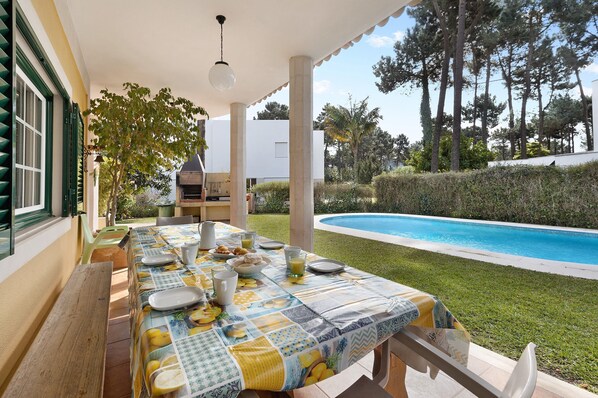 A dining table set outdoors with a pool in the background.