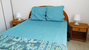 Una cama con un edredón y almohadas azules, flanqueada por dos mesitas de noche de madera con lámparas blancas.
