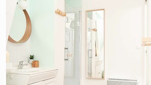 A modern bathroom with a white vanity, a round mirror, a hanging light fixture, and a glass shower enclosure.