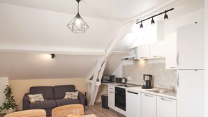 A modern kitchen with white cabinets, a dining area with a wooden table, and a grey sofa.